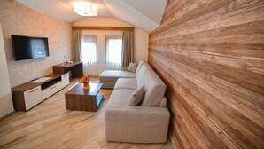 A modern living room with a sectional sofa, a flat-screen TV, wooden flooring, and a large wooden accent wall. - Central Inn (Zlatibor)