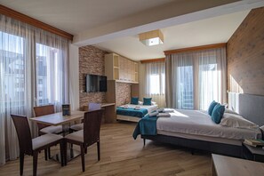 A hotel room with a dining table, two beds, a TV, and a stone accent wall.