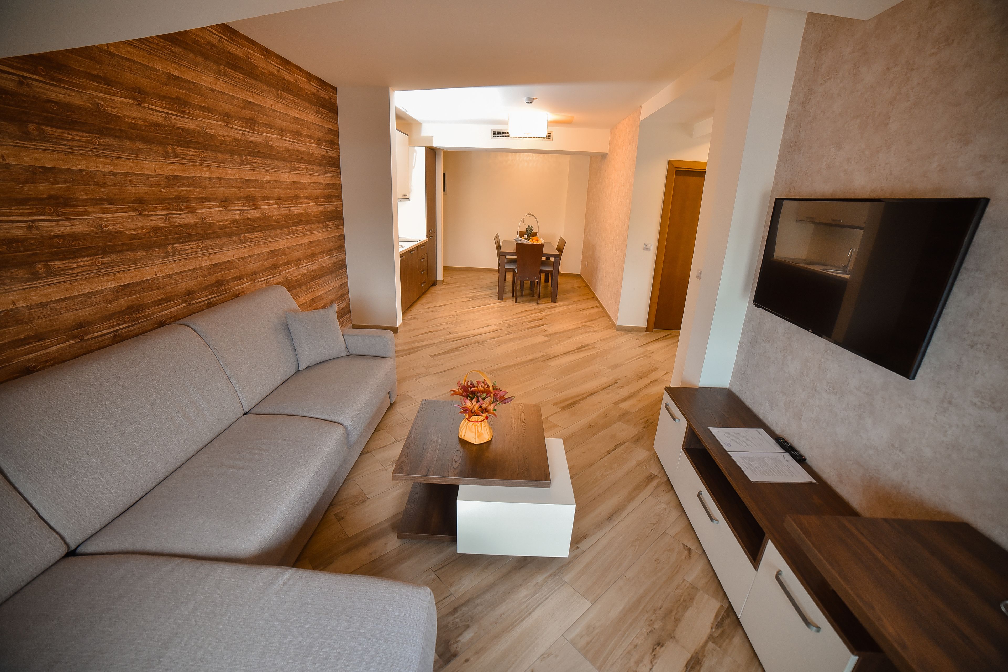En moderne stue med sofa, sofabord med en vase, fjernsyn monteret på væggen og en trævæg.