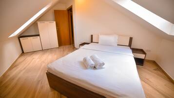 Un dormitorio con techo inclinado, suelo de madera, cama con ropa blanca y un armario.
