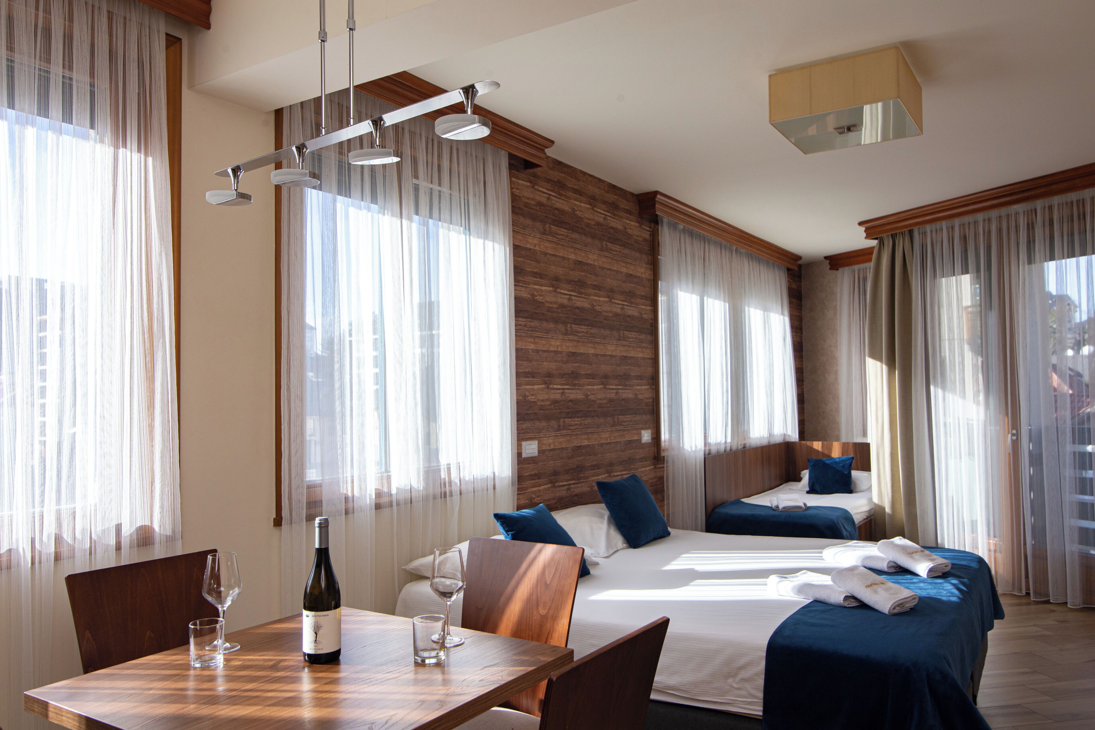A hotel room with two beds, a dining table, and a bottle of wine.