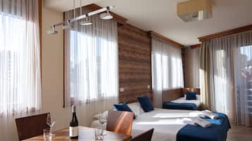 A hotel room with two beds, a dining table, and a bottle of wine.
