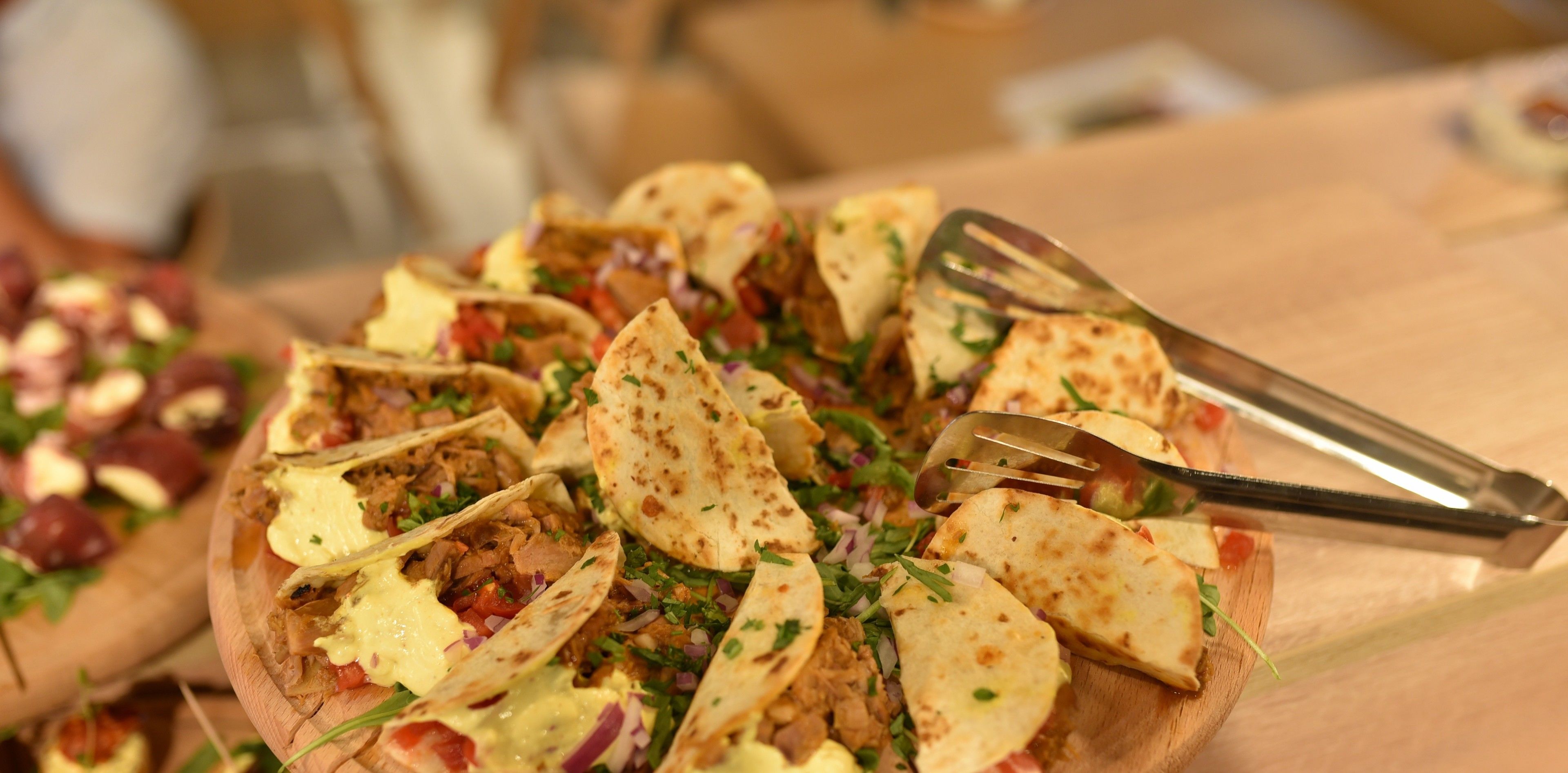 Une planche de service en bois sur laquelle sont disposés divers aliments, notamment des tacos et une fourchette.