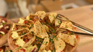 Une planche de service en bois sur laquelle sont disposés divers aliments, notamment des tacos et une fourchette.
