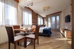 A hotel room with a dining area, a bed, a TV, and large windows.
