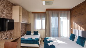 A hotel room with a bed, a desk, a TV, and a view of the city. - Central Inn (Zlatibor)