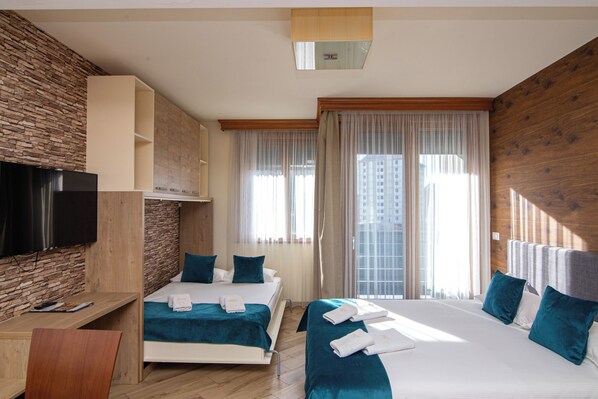 Habitación de hotel con cama, escritorio, televisor y vista a la ciudad.