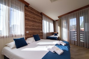 A hotel room with two beds, a wooden wall, and large windows with sheer curtains.