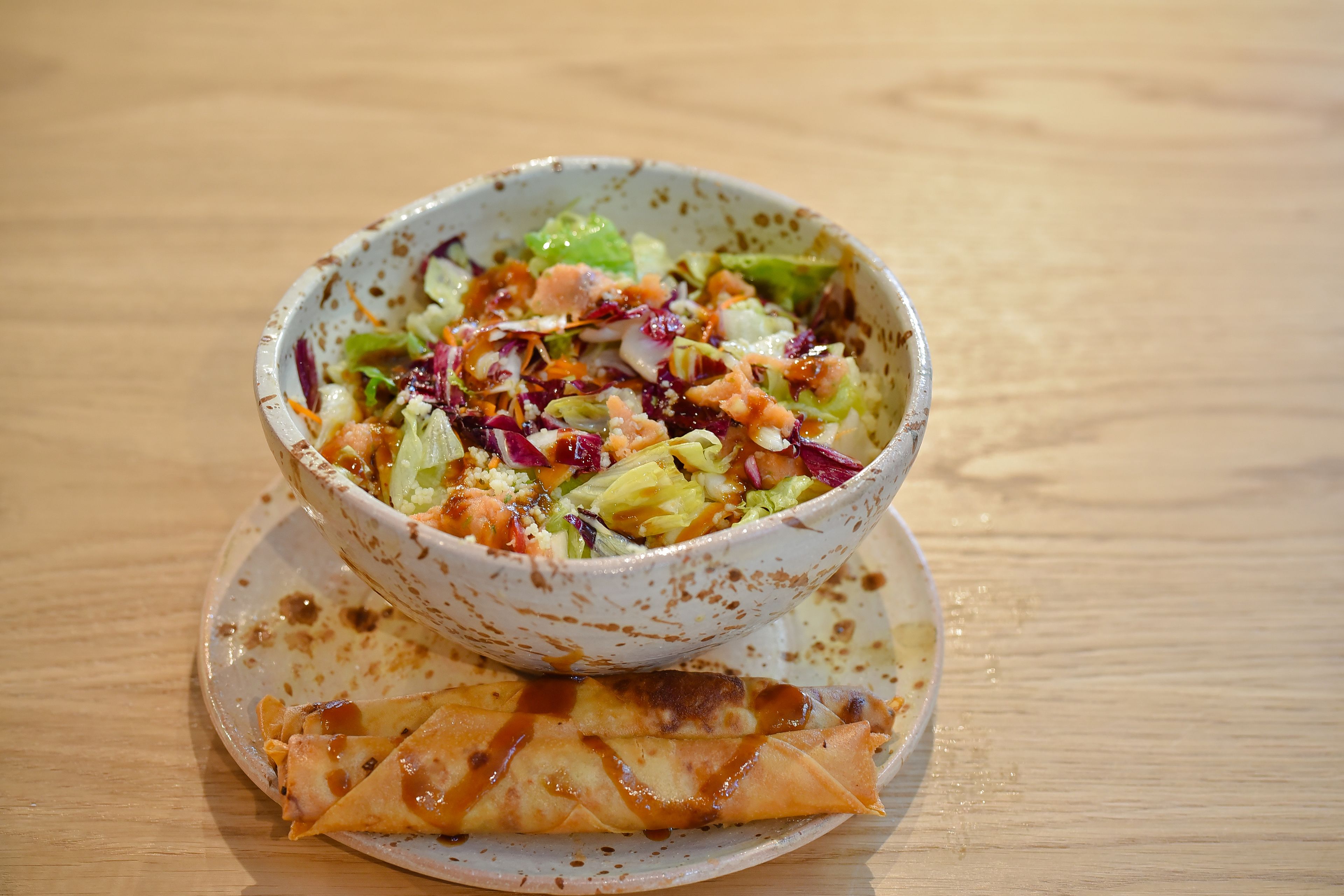 A bowl of salad with a rolled omelette on a plate.