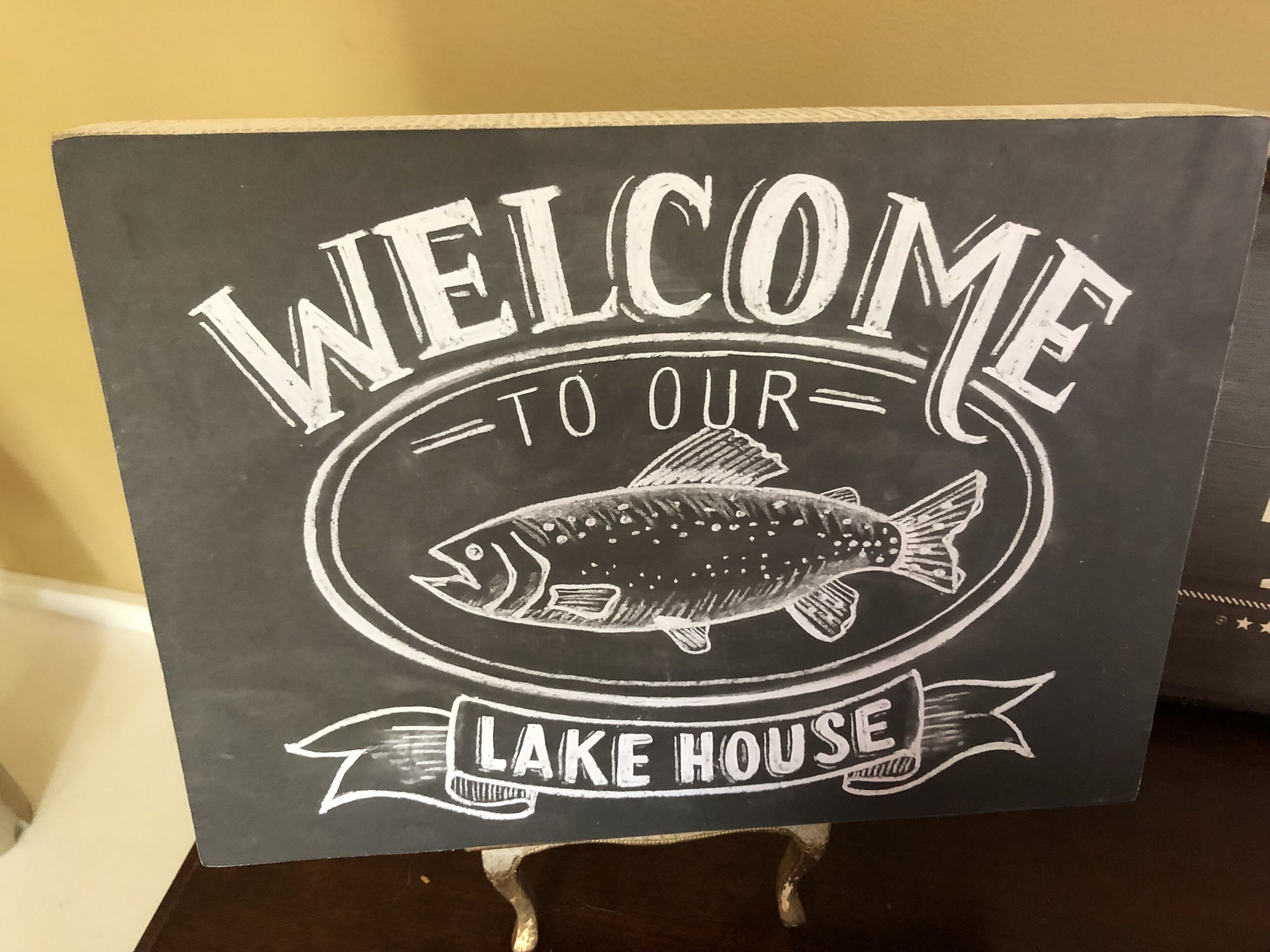 A welcome sign for a lake house with a fish illustration.