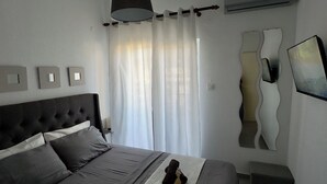 Ein modernes Schlafzimmer mit Bett, Nachttischen, einer Pendelleuchte, einer Wandklimaanlage und einem dekorativen Spiegel.
