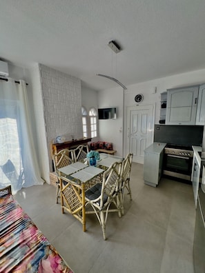 A modern kitchen with built-in appliances, a dining area with wicker chairs, and a TV mounted on the wall.