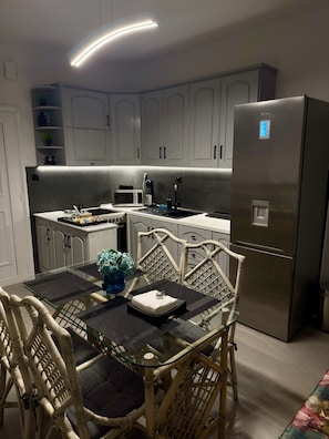 Une cuisine moderne avec des meubles gris, un réfrigérateur en acier inoxydable, une table à manger avec des chaises et un four à micro-ondes.