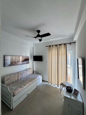 Un soggiorno con divano, ventilatore a soffitto, televisore a schermo piatto e finestra con tende.