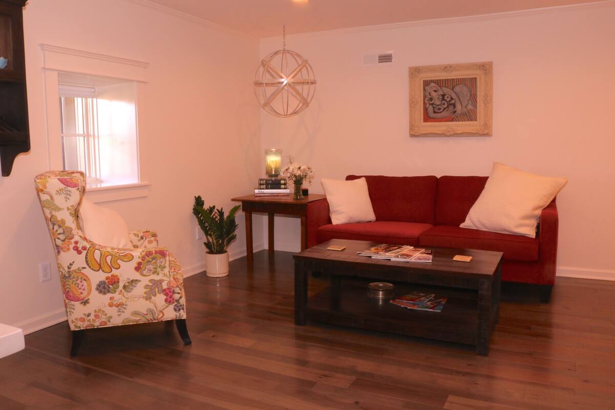 A living room with a red sofa, a floral armchair, a coffee table, and a small side table with a candle and books.