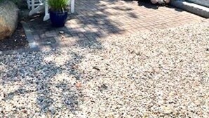 A house with a gravel driveway, two Adirondack chairs, a potted plant, and a flower bed with pink flowers. - Nautical Comfort near Rail Trail (Chatham)