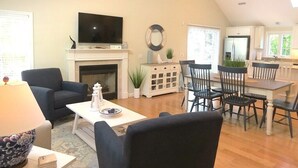 A living room with a fireplace, a television, and a dining area with chairs and a table. - Nautical Comfort near Rail Trail (Chatham)