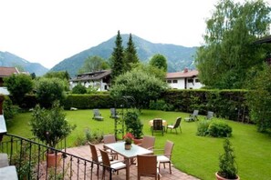 Un espace patio aménagé avec des sièges d’extérieur, une table et des chaises, entouré d’une pelouse bien entretenue et de haies.