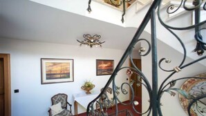 Una escalera con barandillas metálicas decoradas, un candelabro y cuadros en las paredes.