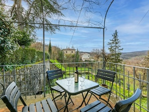 A terrace with a table and chairs, a bottle, and glasses, overlooking a rural landscape with houses and trees. - La Terrazza by Interhome (Radda in Chianti)