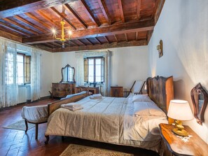 A bedroom with a large bed, wooden ceiling beams, a chandelier, a dresser, a chair, and a desk. - La Terrazza by Interhome (Radda in Chianti)