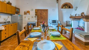 A dining area with a wooden table set for four, surrounded by chairs. A kitchen with wooden cabinets and a stove is visible in the background. - La Terrazza by Interhome (Radda in Chianti)