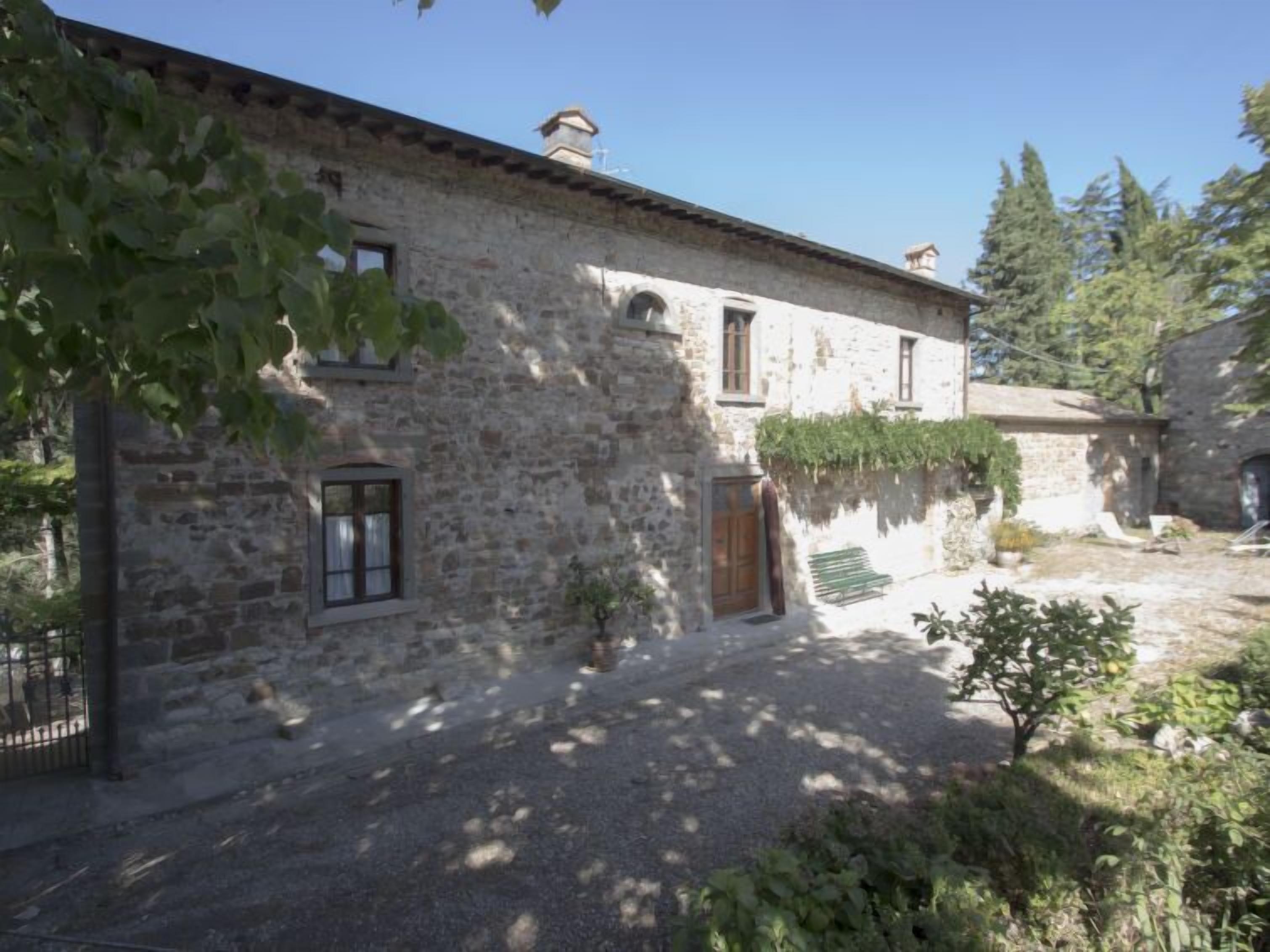 A stone building with a gravel courtyard, a wooden door, and a small garden area.