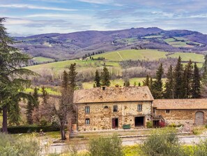 A stone building with a rustic appearance, surrounded by lush greenery and a hilly landscape in the background. - La Terrazza by Interhome (Radda in Chianti)