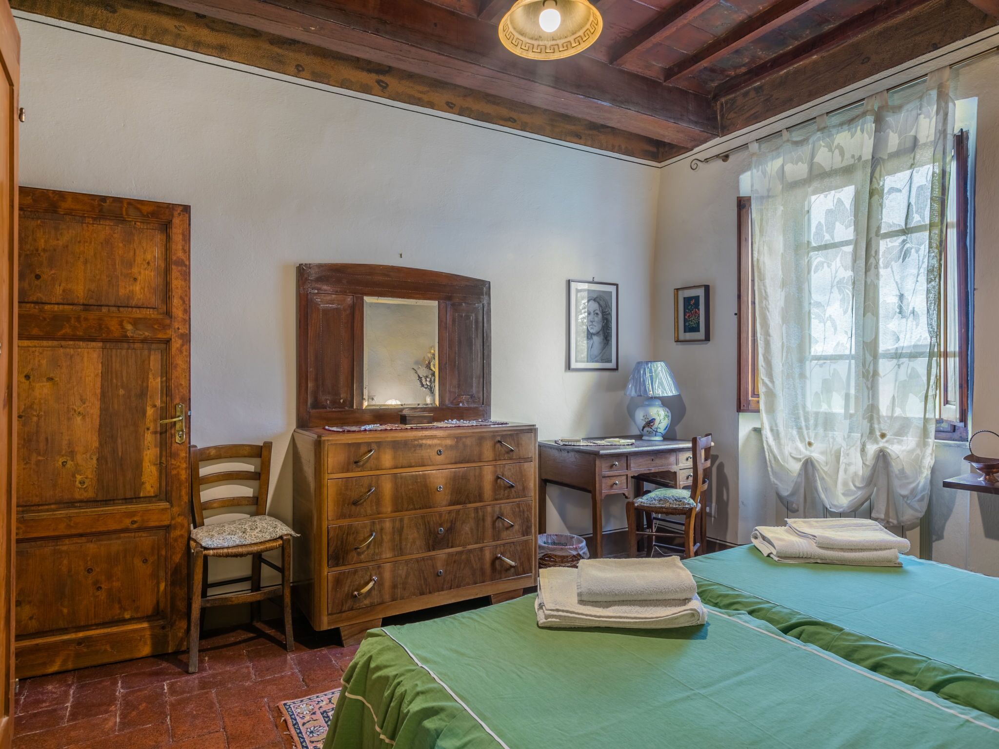 A bedroom with a wooden dresser, a chair, a desk, a lamp, and a bed with green bedding.