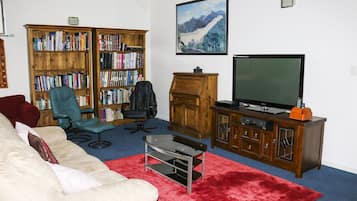 A living room with a sofa, a red rug, a bookshelf, a television, and a wooden cabinet.