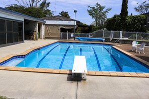 A rectangular swimming pool with a white diving board in the center, surrounded by a concrete deck and a white fence. - The Arches -Ultimate Upper Hunter Getaway- Large Entertainment Living&Relaxation (Singleton)