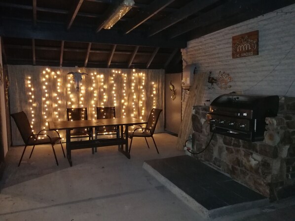 A dining area with a wooden table and chairs, a stone wall with a grill, and string lights. - The Arches -Ultimate Upper Hunter Getaway- Large Entertainment Living&Relaxation (Singleton)