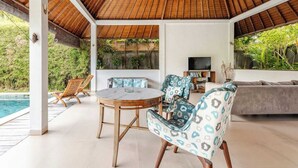A covered outdoor area with a pool, seating, and a television.