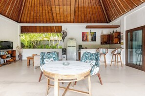Een moderne woonkamer met een ronde tafel, twee stoelen, een televisie en een keukenhoek met kasten en een koelkast.
