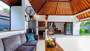 A modern living room with a sofa, a wooden coffee table with fruit, and a fan.