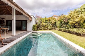 A rectangular swimming pool with a tiled edge, surrounded by a grassy area and dense foliage. - Spacious 1BR Villa in the heart of Seminyak (Seminyak)