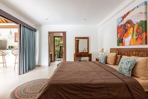 A bedroom with a large bed, a wooden headboard, a painting on the wall, and a view of the outside. - Spacious 1BR Villa in the heart of Seminyak (Seminyak)