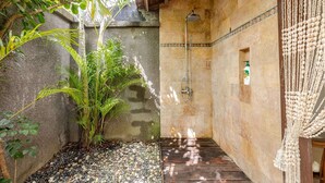 A shower area with a stone wall, a wooden floor, and a hanging macrame decoration.