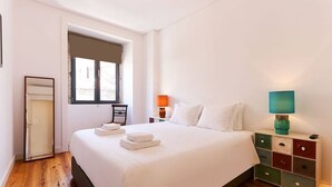 A hotel room with a large bed, a nightstand with a lamp, a window, and a door.