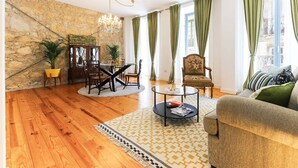 A living room with a stone wall, wooden flooring, a chandelier, a sofa, a chair, a coffee table, and a dining area with a table and chairs.