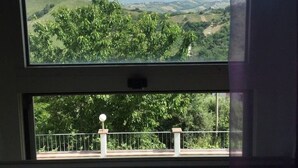 A room with a large window offering a view of a green landscape with hills and trees. - Casa Maya With Private Pool (Serramonacesca)