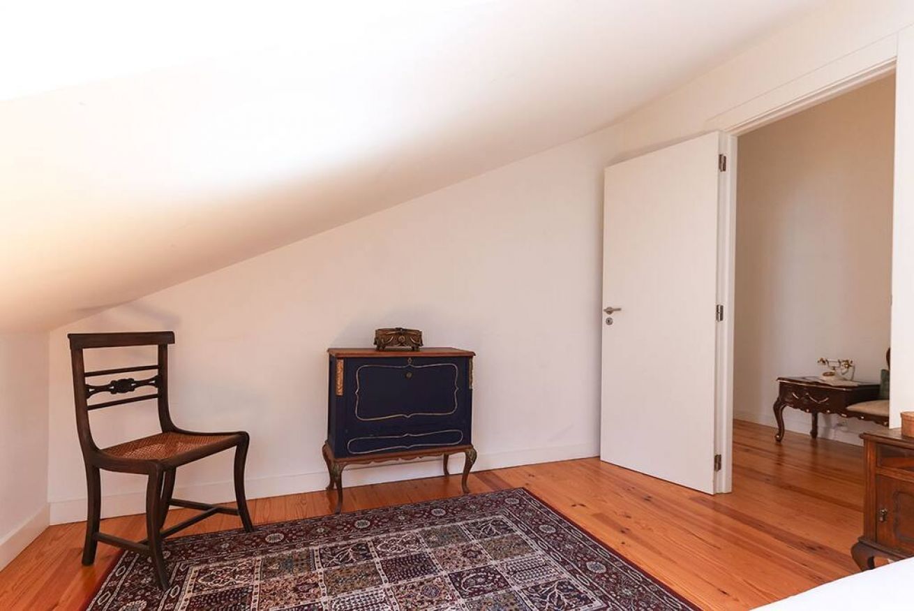 A room with a sloped ceiling, a wooden chair, a small dark blue cabinet, and a patterned rug.