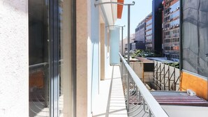 Un balcó amb barana metàl·lica, una porta de vidre i vista sobre un paisatge urbà amb edificis.