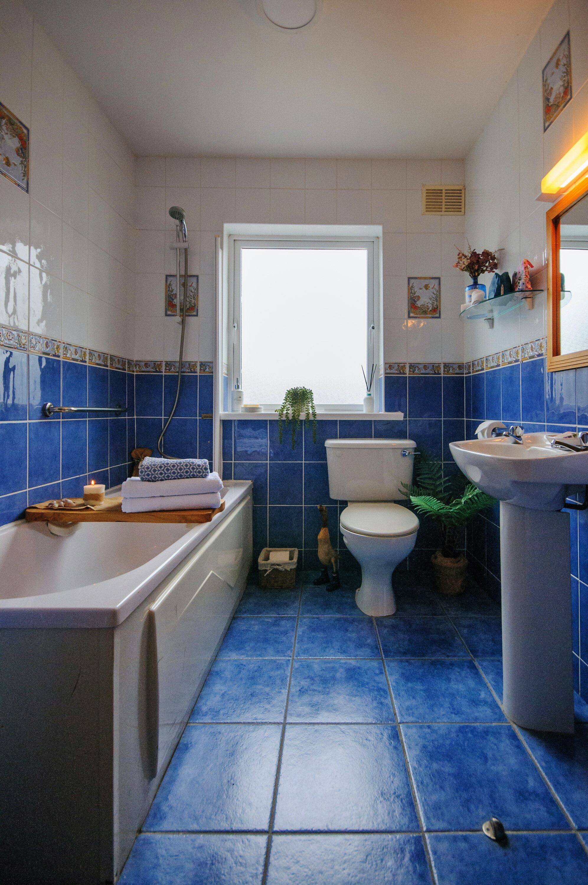 Ein Badezimmer mit Badewanne, Toilette und Waschbecken, mit blauen Fliesen und einem Fenster.