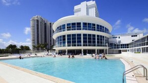 Un hôtel moderne doté d’une piscine circulaire, entourée d’immeubles imposants et de palmiers.