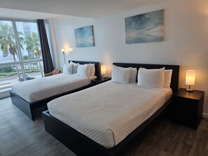 A hotel room with two beds, a large window, and a view of palm trees and buildings.