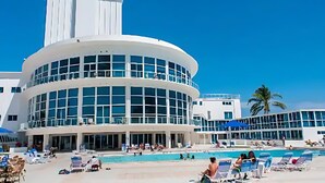 Un hôtel moderne doté d’une grande piscine, de nombreux chaises longues et d’un palmier en arrière-plan.