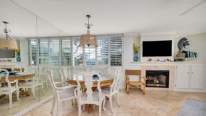 A dining area with a round table and white chairs, a fireplace, and a television mounted above it. - Enjoy Full Resort Access and Ocean Views at KP247! (Saint Simons Island)