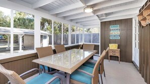 Un patio cubierto con una mesa de vidrio y sillas de mimbre, rodeado de paredes de madera y ventanas amplias.