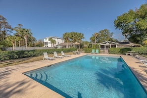 A rectangular swimming pool with clear blue water, surrounded by lounge chairs and a small gazebo.